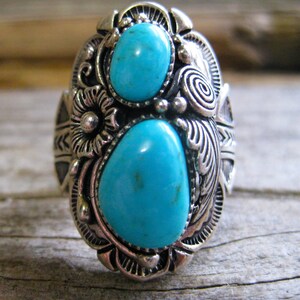 May include: A silver ring with two turquoise stones set in a detailed floral design.