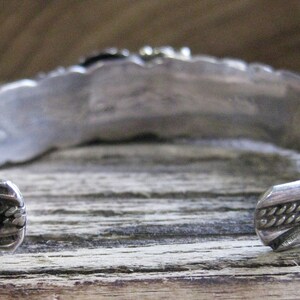 May include: Silver bracelet with intricate designs on the back. The bracelet is open and has a braided design on one end.