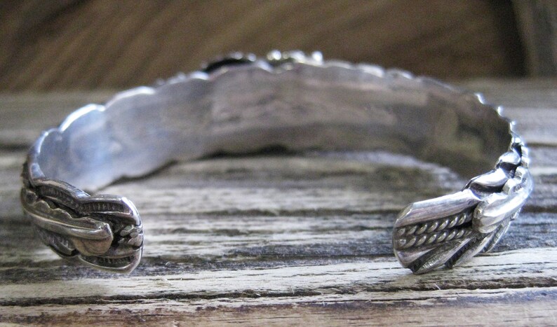 May include: Silver bracelet with intricate designs on the back. The bracelet is open and has a braided design on one end.