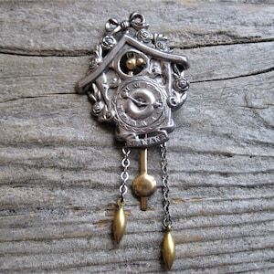 May include: Silver and gold cuckoo clock charm with a swinging pendulum and a clock face that reads "MANANA".