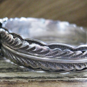 May include: A silver bracelet with a feather design. The bracelet is made of sterling silver and has a detailed feather pattern.