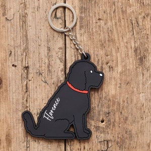 以下が含まれることがあります： 座っている犬の形をした黒いゴム製のキーホルダー。犬は赤い首輪をしていて、側面に「フローレンス」という名前が書かれています。