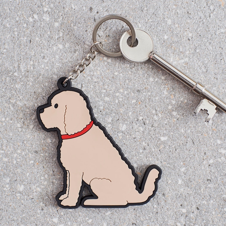 以下が含まれることがあります： 銀色のキーリングとキーに付けられた、赤い首輪をしたベージュの犬のキーホルダーです。