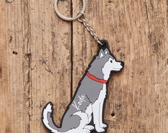 May include: A keychain featuring a cartoon husky dog in gray, white, and black, with a red collar. The dog is sitting, and the name "Koda" is written on its side. The keychain has a silver ring and chain.