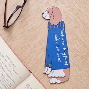 May include: A blue and brown bookmark shaped like a dog wearing a blue sweater. The bookmark has the text "Thank you for being the best Teacher. Love Leo XXX" written on it.
