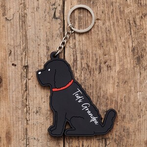以下が含まれることがあります： 赤い首輪をした犬の形をした黒いゴム製のキーホルダー。キーホルダーには「Ted's Grandpa」という文字が書かれています。