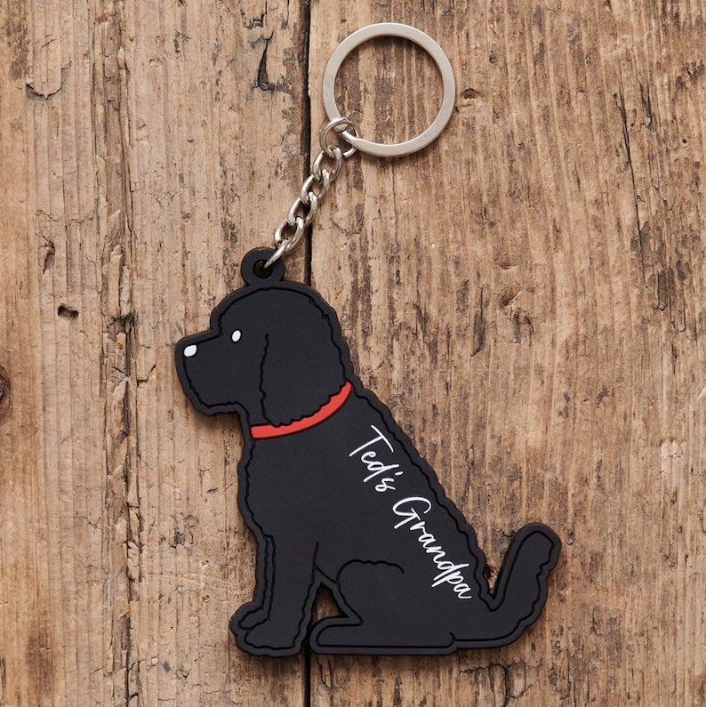 以下が含まれることがあります： 赤い首輪をした犬の形をした黒いゴム製のキーホルダー。キーホルダーには「Ted's Grandpa」という文字が書かれています。