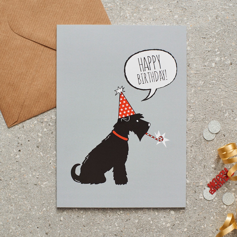 May include: A birthday card with a black dog illustration wearing a party hat and holding a party favor. The card has the words "HAPPY BIRTHDAY!" in a speech bubble. A brown envelope and confetti are also visible.