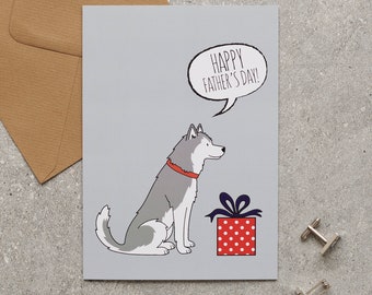 Könnte beinhalten: Eine Vatertagskarte mit einem Cartoon-Husky-Hund mit rotem Halsband, neben einer roten Geschenkbox mit weißen Punkten. Die Karte zeigt "HAPPY FATHER'S DAY!" in einer Sprechblase. Enthält einen braunen Umschlag und silberne Manschettenknöpfe.