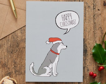 Könnte beinhalten: Eine graue Weihnachtskarte mit einem Cartoon-Husky, der einen roten Weihnachtsmann-Hut trägt. Der Husky schaut nach rechts und hat eine Sprechblase über seinem Kopf, auf der "Frohe Weihnachten!" steht.