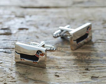 May include: A pair of silver cufflinks with a black and orange dachshund design.