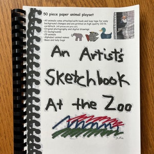May include: A white booklet with a black spiral binding. The cover features a colorful illustration of a zoo with the title "An Artist's Sketchbook At the Zoo" and the text "50 piece paper animal playset".