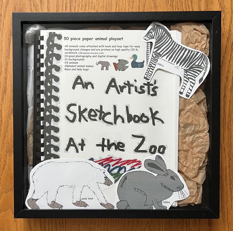 May include: A black framed sketchbook with the title "An Artist's Sketchbook At the Zoo" and a variety of animal stickers, including a zebra, polar bear, and rabbit.