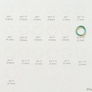 May include: A white card with a grid of circles labeled with ring sizes in millimeters. The sizes range from 5 to 14, with half sizes included. A green rubber ring is shown next to the size 10 1/2 circle.
