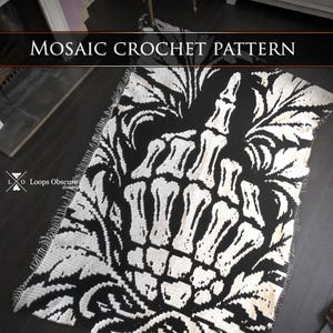 Könnte beinhalten: Eine rechteckige schwarz-weiße Mosaik-Häkeldecke mit einer zentralen Grafik einer Skeletthand, die den Mittelfinger zeigt, umgeben von verzierten Blattmustern. Der Text MOSAIC CROCHET PATTERN ist oben im Bild zu sehen.