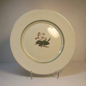 May include: A white ceramic dinner plate with a gold rim and a green and gold floral design in the center.