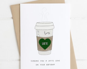 May include: A white coffee cup with a brown sleeve and a green heart that says "LATTE" on it. The cup has steam coming out of the top and the name "Lucy" written on the side. The text below the cup says "Sending you a latte love on your birthday."