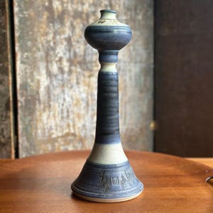 May include: A tall, handcrafted ceramic vase with a bulbous top and a slender, cylindrical body. The vase features a color palette of blue, cream, and brown, with textured detailing and a flared base. The vase stands approximately 12 inches tall.