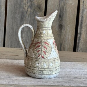 May include: A small, cream-coloured ceramic jug with a red and white leaf design. The jug has a handle and a spout.