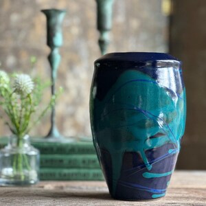 May include: A blue and green ceramic vase with a glossy finish. The vase has a rounded, oval shape and is decorated with abstract blue and green lines.