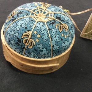 Pode incluir: Uma caneca de cerâmica branca com uma alça preta e o texto "But First, Coffee" em negrito preto. A caneca está sobre um fundo desfocado, sugerindo um ambiente acolhedor.