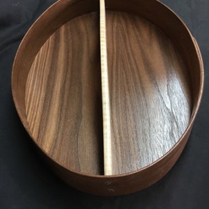 Puede incluir: Una caja redonda de madera con un divisor claro. La caja est&aacute; hecha de madera marr&oacute;n oscuro con un borde marr&oacute;n m&aacute;s claro. El interior tiene un patr&oacute;n de vetas de madera natural. El divisor es de color madera clara natural.