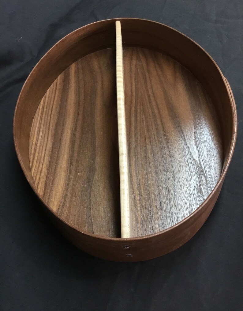 Puede incluir: Una caja redonda de madera con un divisor claro. La caja est&aacute; hecha de madera marr&oacute;n oscuro con un borde marr&oacute;n m&aacute;s claro. El interior tiene un patr&oacute;n de vetas de madera natural. El divisor es de color madera clara natural.