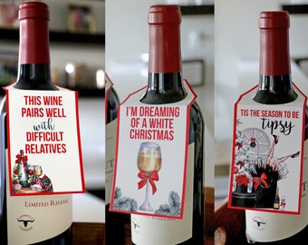 May include: Three wine bottles with decorative paper tags hanging from the necks. The tags feature red and black text reading "THIS WINE PAIRS WELL WITH DIFFICULT RELATIVES," "I'M DREAMING OF A WHITE CHRISTMAS," and "TIS THE SEASON TO BE TIPSY."