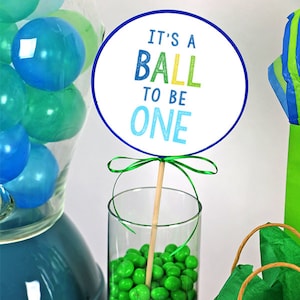 印刷可能な青と緑の「It&#39;s a Ball To Be ONE」センターピーススティック、1歳の誕生日ボールケーキトッパー、Turning ONE is a Ballパーティーデコレーション
