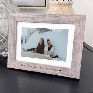 May include: A gray wood picture frame with a white mat and a photo of two people sitting on a bench. The frame has the text "True friendship knows no distance" engraved on the bottom.