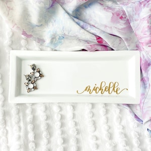 May include: White rectangular ceramic tray with a gold inscription that reads "michelle".  A pair of crystal earrings are on the tray.