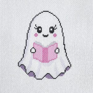 May include: A cross-stitch pattern on white fabric featuring a white ghost with black eyes, pink cheeks, and a pink book. The ghost has a purple hem. The letters EAD are stitched in black in the bottom right corner, with a color key on the left.