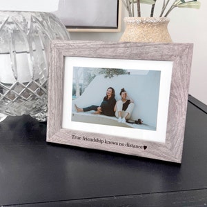 K&ouml;nnte beinhalten: Ein grauer Holzrahmen mit einem Foto von zwei Frauen, die auf einer Bank sitzen. Der Rahmen tr&auml;gt den Text "True friendship knows no distance", der unten eingraviert ist.