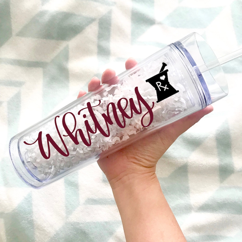 May include: A clear plastic tumbler with a maroon inscription that reads "Whitney" and a black and white mortar and pestle with a heart and the letters "Rx".