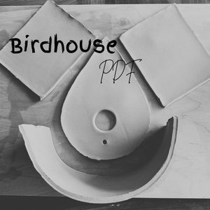 May include: A set of white ceramic birdhouse pieces, including a roof, a base, and a front panel with a hole for the birdhouse entrance. The pieces are arranged on a wooden surface. The text "Birdhouse PDF" is written on the front panel.
