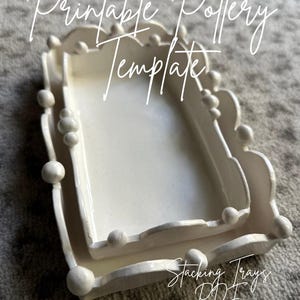 Könnte beinhalten: Zwei weiße, stapelbare Keramiktabletts mit gewellten Kanten und dekorativen Kugelakzenten. Die rechteckigen Tabletts sind ineinander verschachtelt, mit dem Text "Printable Pottery Template" und "Stacking Trays PDF" in Schreibschrift.