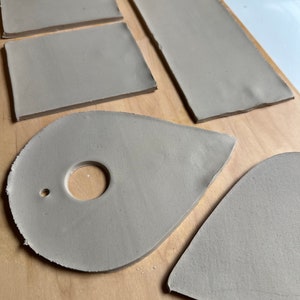 May include: Five pieces of gray clay, two rectangular, one teardrop shaped with a hole, one oval shaped with a hole, and one heart shaped.