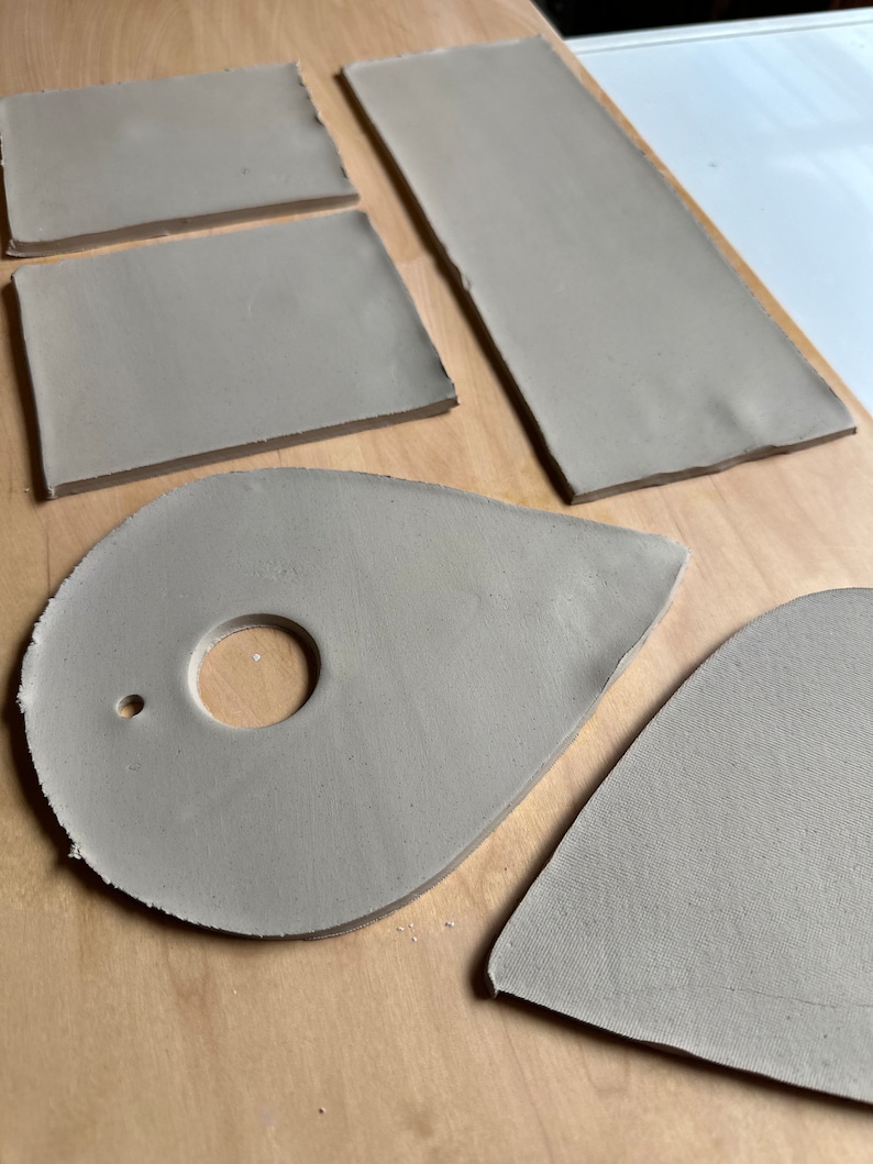 May include: Five pieces of gray clay, two rectangular, one teardrop shaped with a hole, one oval shaped with a hole, and one heart shaped.