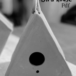 May include: A grey triangular ceramic birdhouse with a round hole for the birds to enter. The birdhouse has a small handle on the top and a small hole on the bottom. The text "Bird house Pdf" is written on the image. The text "Printable pottery template" is written below the birdhouse.