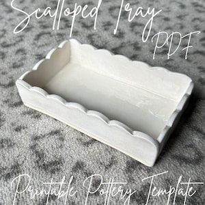 Può includere: Vassoio bianco in ceramica con bordi a festoni, un modello di ceramica stampabile. Il vassoio è su un tappeto grigio. Il testo "Scalloped Tray PDF" è scritto in corsivo nero sopra il vassoio.