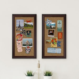 May include: Two cork boards with brown frames, each filled with various travel-themed photos, postcards, and stickers. The left board features a photo of the Eiffel Tower, a photo of the Taj Mahal, and a sugar skull sticker. The right board features a photo of a couple standing in front of a lake, a photo of a woman riding a bicycle, and a "Keep Calm and Carry On" sticker.