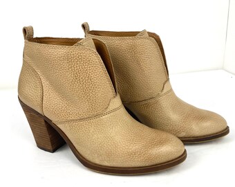 May include: A pair of beige leather ankle boots with a pointed toe and a block heel. The boots have a v-shaped opening at the top of the shaft.
