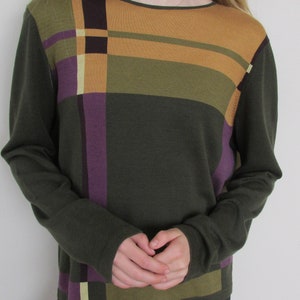 Puede incluir: Un suéter de manga larga con un patrón de cuadros en tonos de verde, morado, amarillo y marrón.