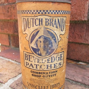 May include: An antique cylindrical container with a rusty metal lid. The label reads "DUTCH BRAND BEVEL-EDGE PATCHES" with a vintage illustration. The container is tan with blue and white accents and text. The text "VAN CLEEF BROS" is also visible.