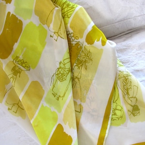 Peut inclure: Un foulard en soie plié avec un motif de rectangles jaunes et chartreuse et des dessins au trait de personnages. Le foulard a un fond blanc et une bordure jaune. Le tissu est drapé sur une surface blanche.