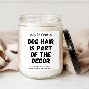 May include: A white soy candle with a black label that reads "Lucky You Candle Co. Dog Hair Is Part Of The Decor 8oz/227g Soy Candle Hand-Poured In Telford, PA"