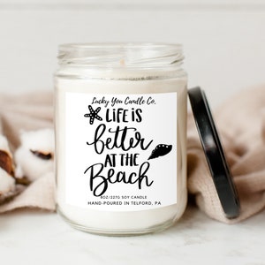May include: A white candle jar with a black label that reads "Lucky You Candle Co. Life is better at the Beach" with a starfish and seashell graphic. The candle is 8 oz/227g and hand-poured in Telford, PA.