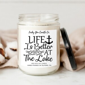 May include: A white soy candle in a glass jar with a black lid. The label reads "Lucky You Candle Co. LIFE is Better AT The Lake 8oz/227g Soy Candle Hand-Poured in Telford, PA".