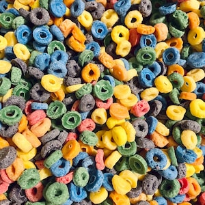 May include: A close-up of a bowl filled with colorful cereal rings. The cereal is a mix of blue, green, yellow, orange, and red rings.