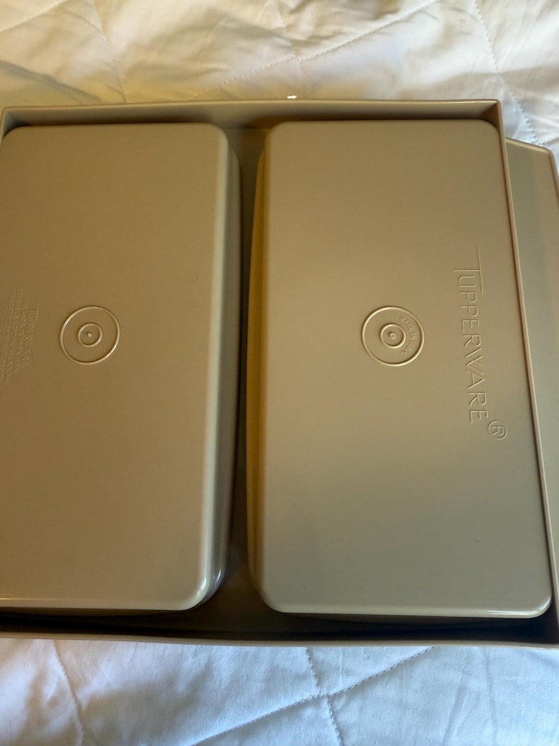 May include: Two beige rectangular Tupperware containers with rounded corners are nested in a matching tray. Each container has a circular indentation in the center. The Tupperware logo is visible on one container.